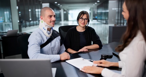 Injured worker wearing neck brace meets with woman and lawyer at desk