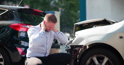 Male driver crouching beside damaged car after collision with another vehicle
