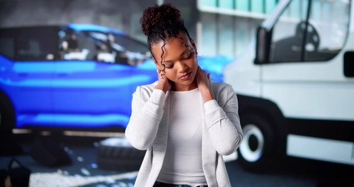 Woman holding neck beside damaged vehicles after collision scene